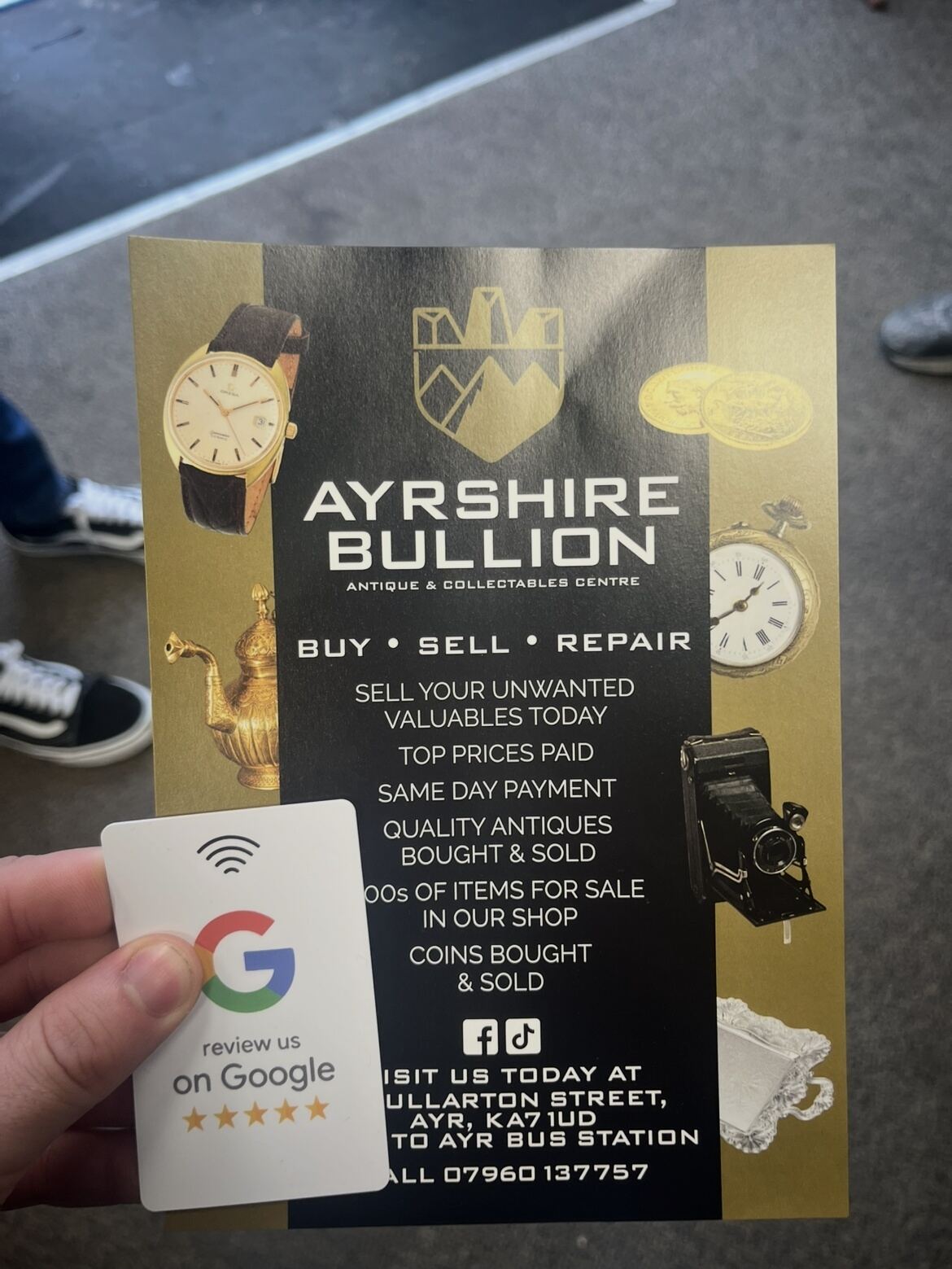 NFC review card held up against Ayrshire Bullion's shop signage